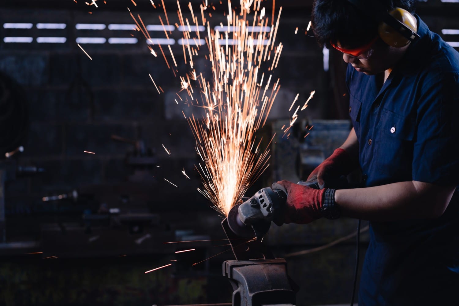 A man grinds metal, creating a shower of sparks in a workshop setting, showcasing craftsmanship and precision.