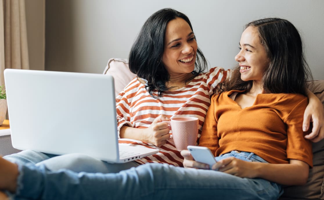 Two women seated on a couch, engaged with a laptop, sharing ideas and collaborating in a comfortable setting.