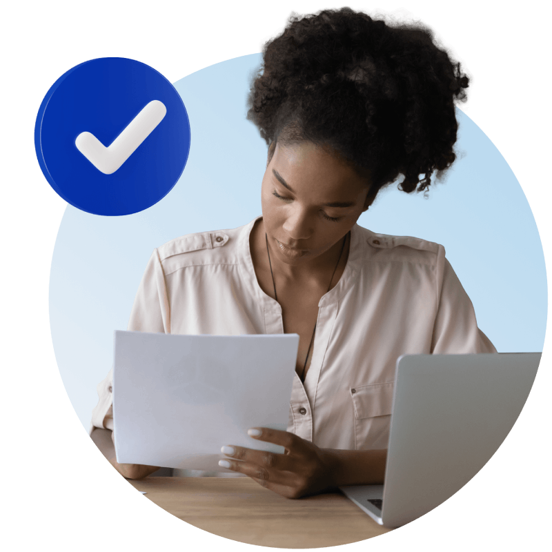 A woman sitting at a table, focused on her laptop while holding a check in her hand, symbolizing financial management.
