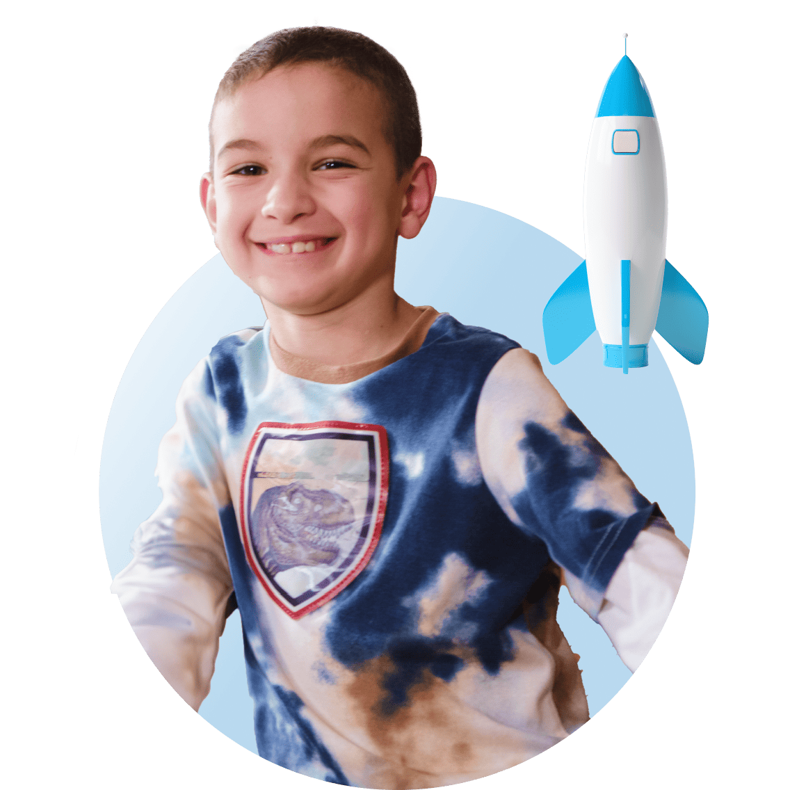 A boy wearing a colorful tie-dye shirt featuring a rocket design, smiling and standing outdoors.